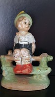 Antique ceramic boy figure sitting on a fence.