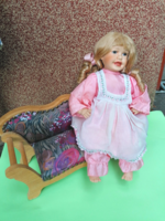 Old porcelain doll on a large wooden upholstered sofa