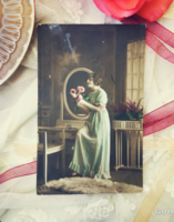Antique postcard with a lady holding a bouquet of flowers in front of a mirror