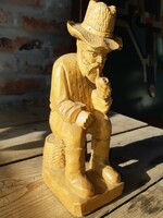 A wooden statue of a peasant smoking a pipe