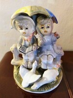 Porcelain sculpture, children sitting on a fence with umbrellas and geese