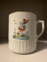 A normal-sized mug with a fairy tale pattern, with a little girl and a kitten, marked, but unfortunately less legible.