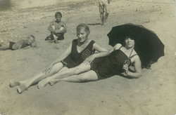Sunbathing ladies on the beach with parasols and onlookers. Original paper image.