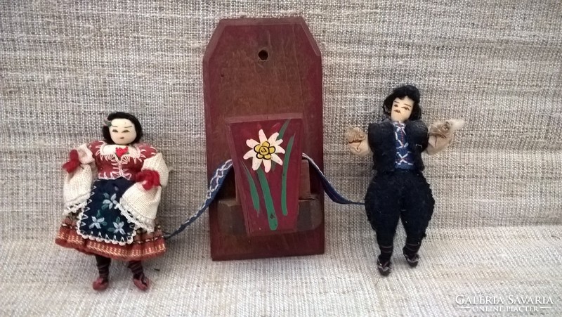A snow-covered wall ornament on a wooden sheet with two dolls in folk clothes