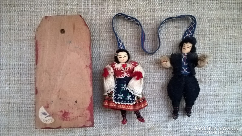 A snow-covered wall ornament on a wooden sheet with two dolls in folk clothes