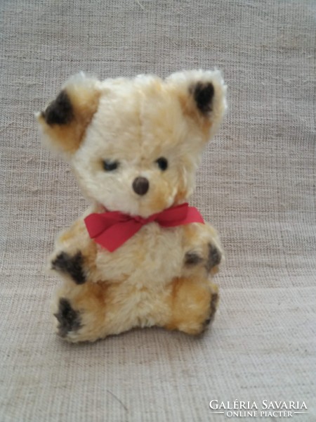 Old wool small teddy bear with glass eyes with a red ribbon around its neck