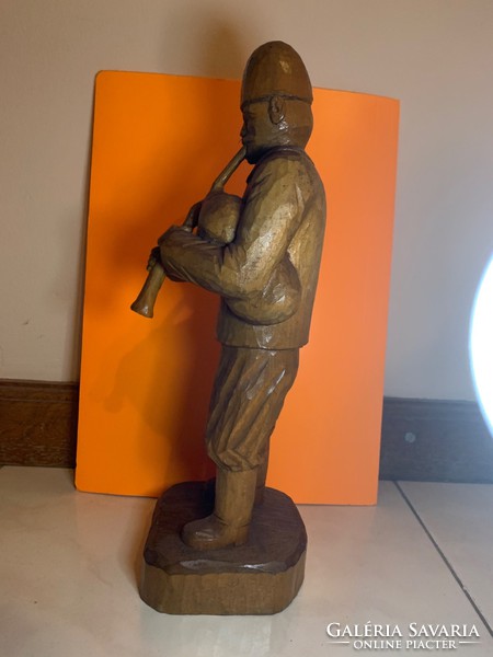 A carved wooden statue of a man playing a flute, 30 cm high