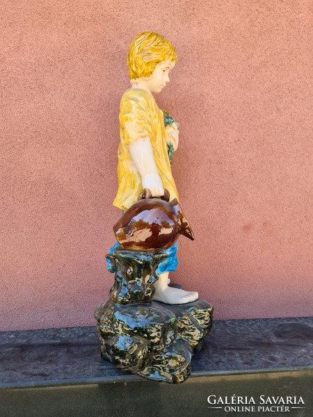 A large majolica boy holding a bouquet of flowers and a jug