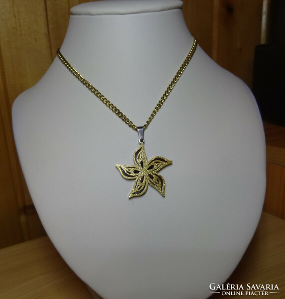 Pendant and chain made of surgical steel in the shape of a flower, with wavy petals sprinkled with golden sand.