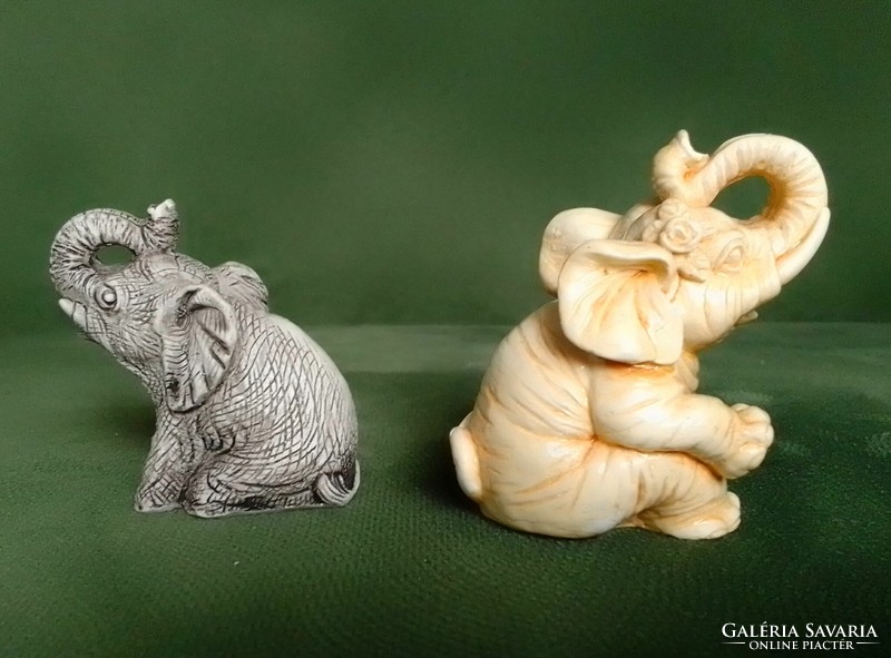 Two lucky sitting polyresin elephant figurines with raised trunks are hand painted