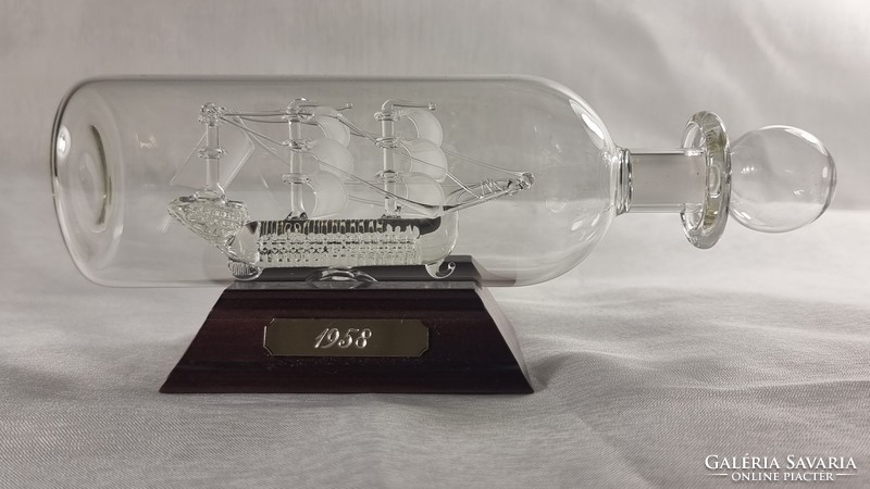 A meticulously made glass ship blown into a blown glass. Copper engraved with the year 1958. On a wooden pedestal