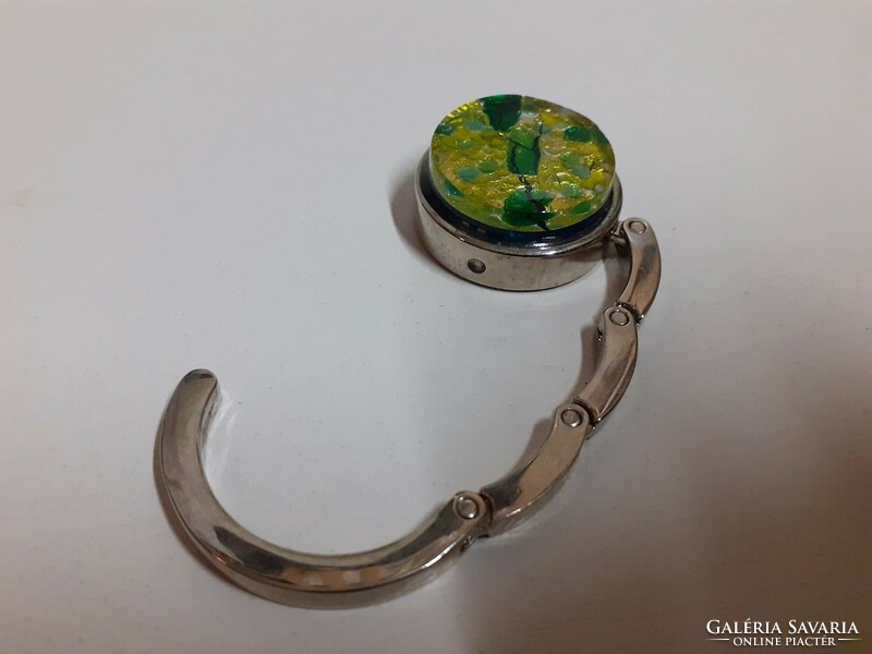 A steel folding bag in good condition hanging on the edge of a table, encrusted with a green stone