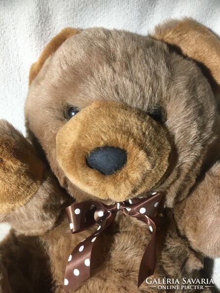 A big, long-furred teddy bear with a pocket on the back with the inscription 