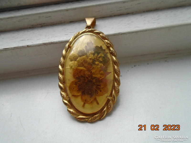 An oval dried flower pendant in a gilded frame with a porcelain back under a convex glass