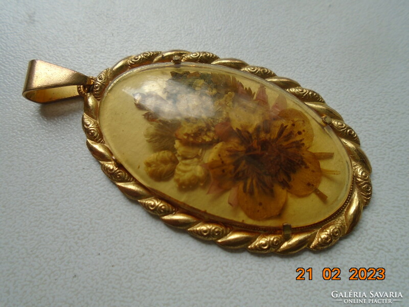 An oval dried flower pendant in a gilded frame with a porcelain back under a convex glass