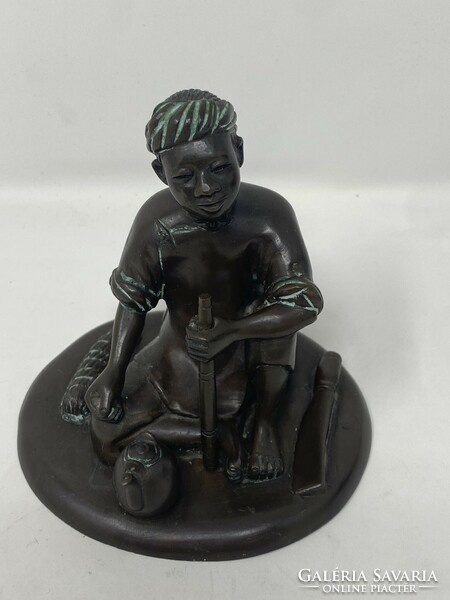 Marked bronze statue of an Indonesian boy sitting on the ground, smoking a pipe and drinking tea, c