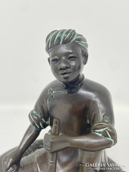 Marked bronze statue of an Indonesian boy sitting on the ground, smoking a pipe and drinking tea, c