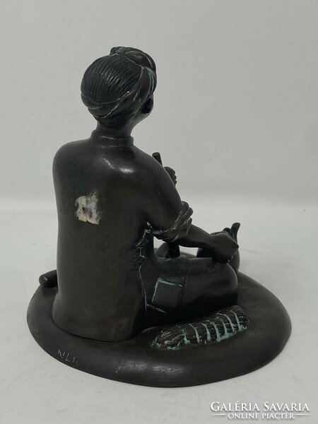 Marked bronze statue of an Indonesian boy sitting on the ground, smoking a pipe and drinking tea, c