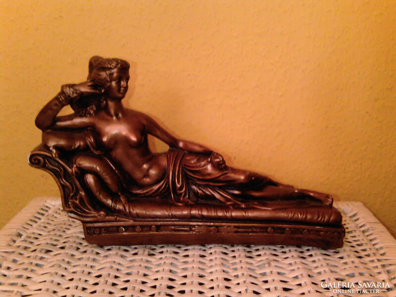 Female nude sculpture lying on a bronze-colored sofa