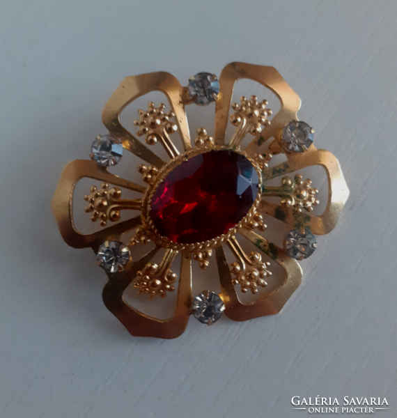 A gilded pin in the center of a large red polished stone circle adorned with white set glass stones