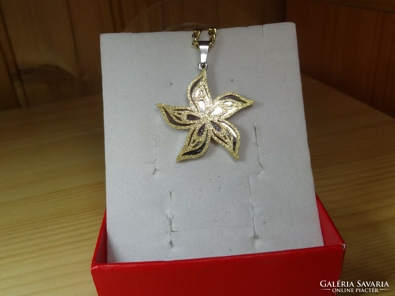 Pendant made of surgical steel in the shape of a flower with wavy petals. The surface of the flower is gold colored and grainy.