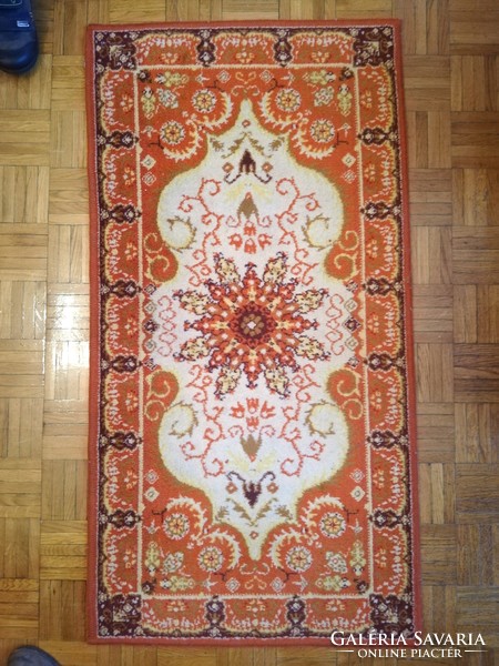 A small machine-made Persian carpet in an orange tone, a legacy of Inke László and Márta