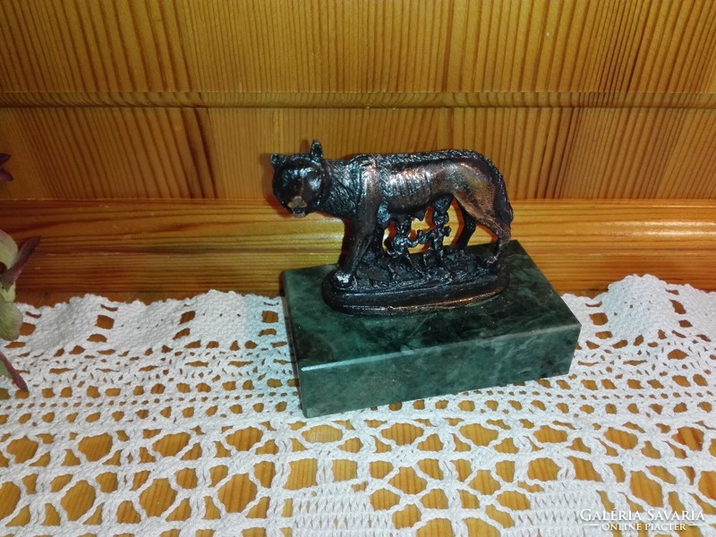 Red copper statue of Romulus and Remus on a marble plinth.