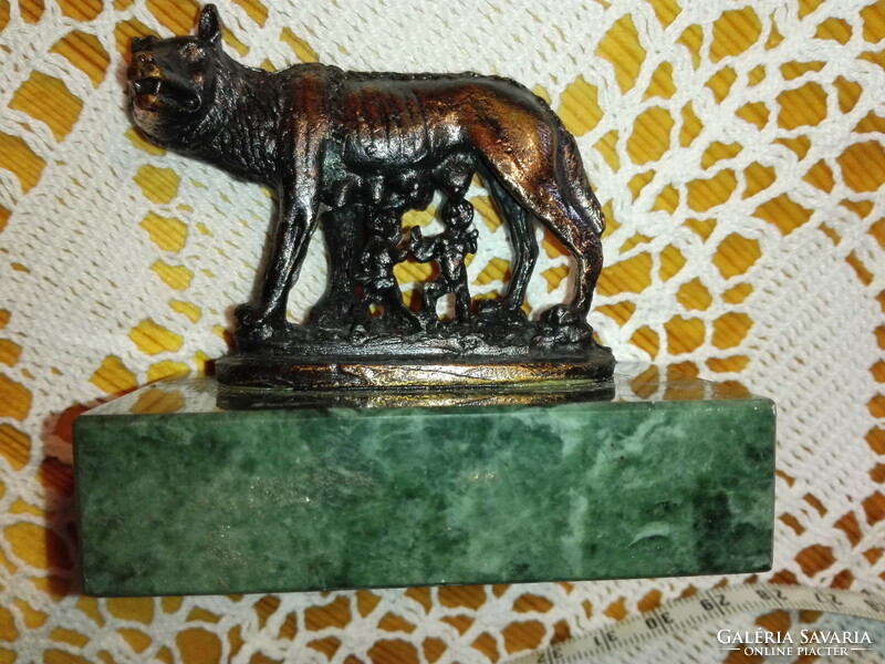 Red copper statue of Romulus and Remus on a marble plinth.