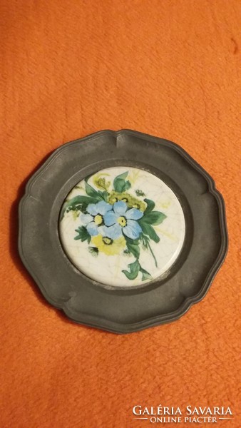 A small pewter plate with a floral porcelain insert that can be hung on an old wall