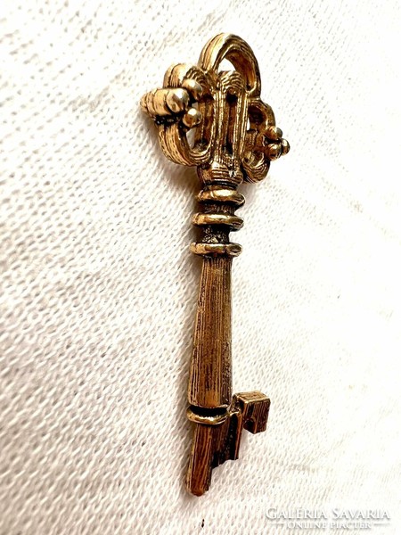 A miniature replica of a gold-colored bizsu church door key, a legacy of Inke László