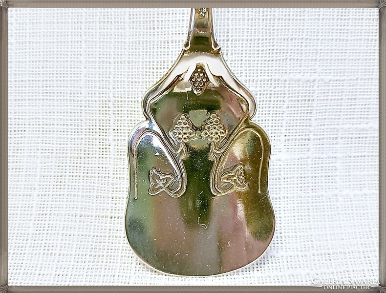 A decorative, silver-plated English souvenir teaspoon, with a beautiful grape pattern in the material.