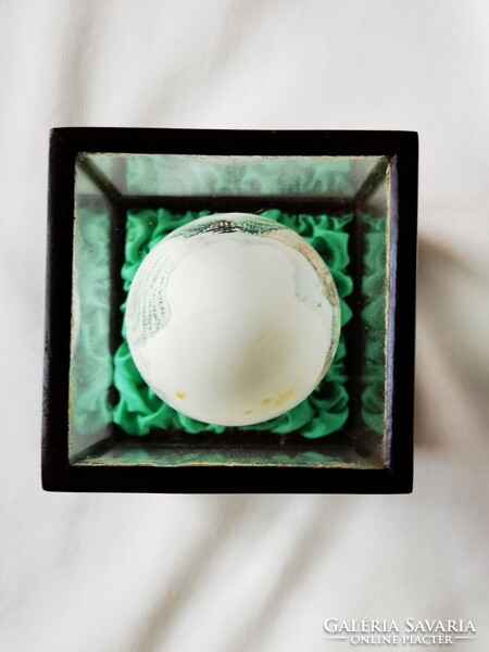 Old Chinese hand-painted egg in wooden holder behind glass