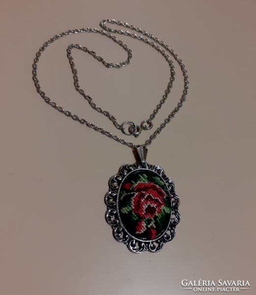 A silver-colored necklace with a pendant decorated with tapestry in a filigree silver-colored frame