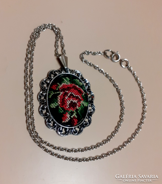 A silver-colored necklace with a pendant decorated with tapestry in a filigree silver-colored frame