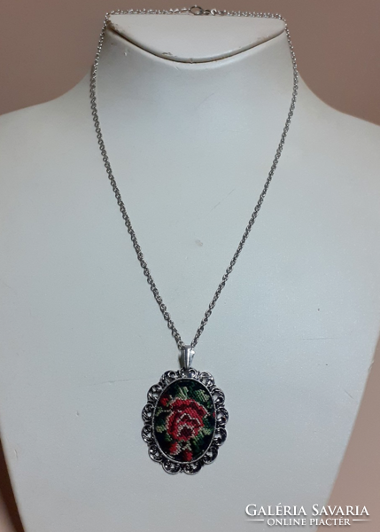 A silver-colored necklace with a pendant decorated with tapestry in a filigree silver-colored frame