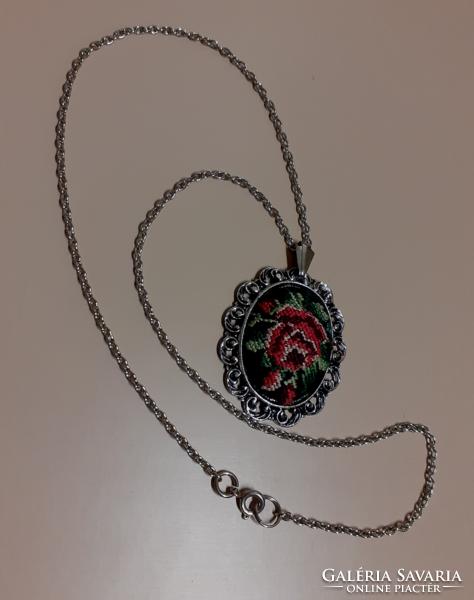 A silver-colored necklace with a pendant decorated with tapestry in a filigree silver-colored frame