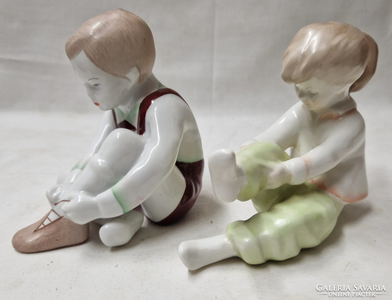 Aquincumi boy tying his shoes and girl pulling her socks porcelain figurines together in perfect condition