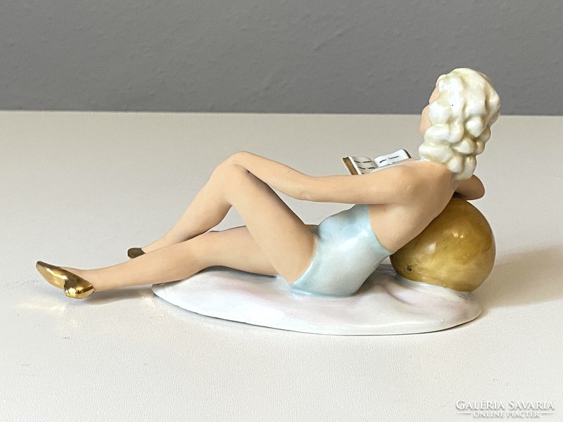 Painted German porcelain statue of a girl reading and sunbathing leaning on a ball