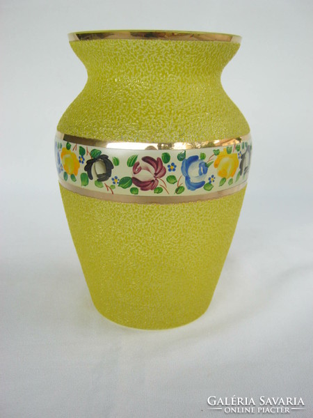 A yellow glass vase with a thick rough surface decorated with a flower painted in a circle